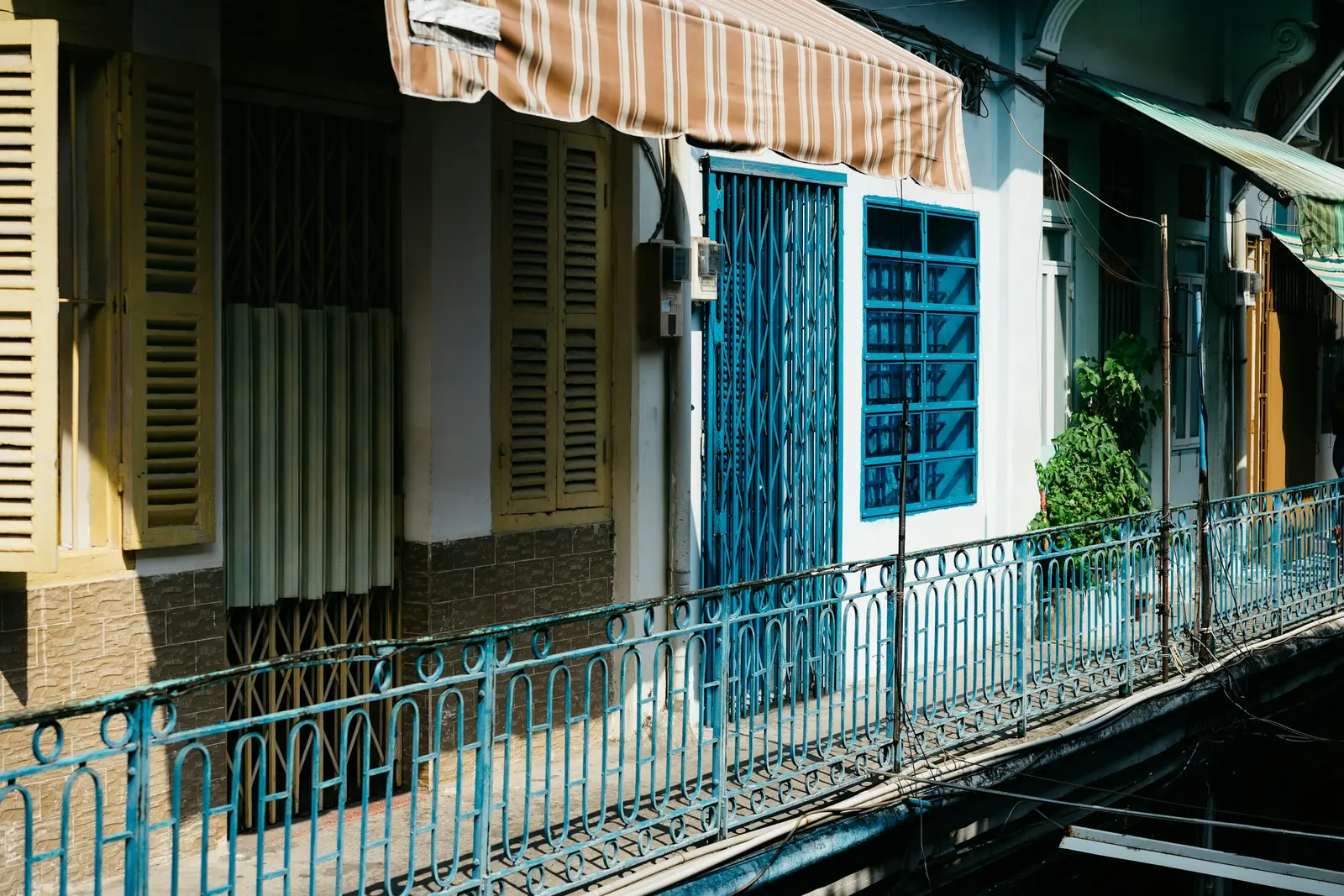 Striped fabric awning shading a balcony with blue shutters and railings