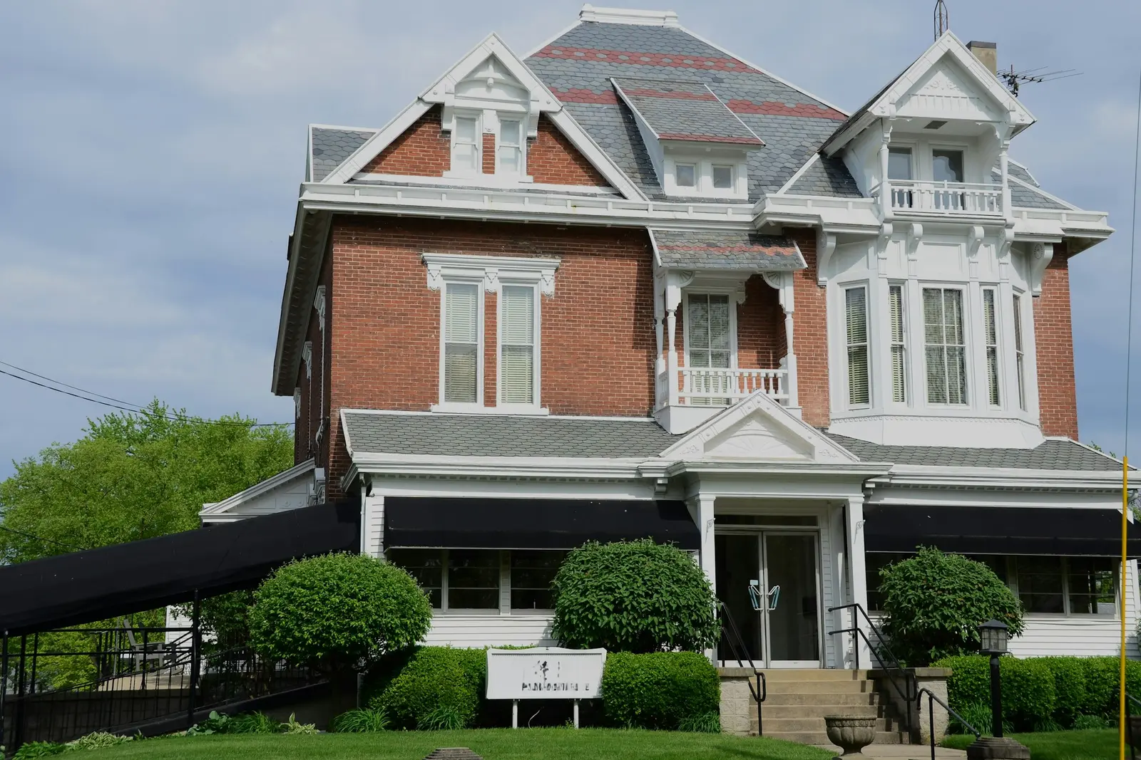 Red-brick house with dark awnings along its ground-floor porch