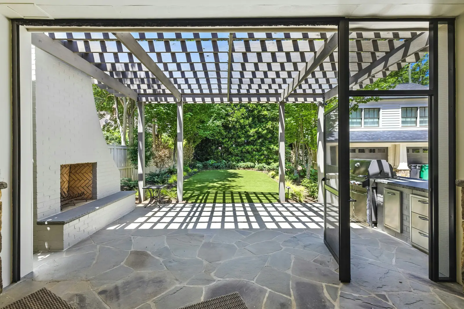 Pergola with a slatted roof over a stone patio and outdoor kitchen